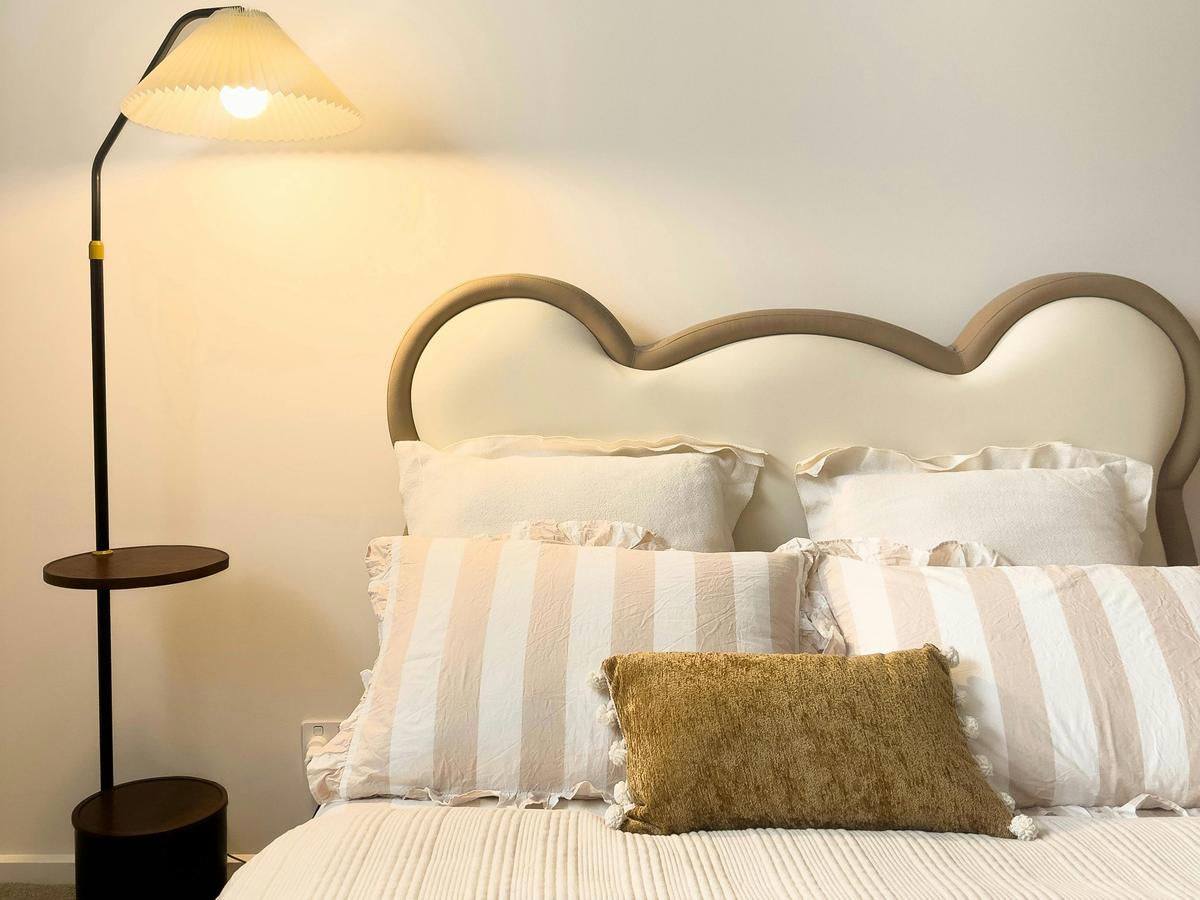 Bedroom with a neatly made double bed, pillows and a floor lamp.