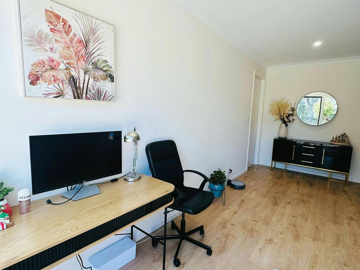 Home office with a desk, computer monitor, office chair and wall art in a bright room.