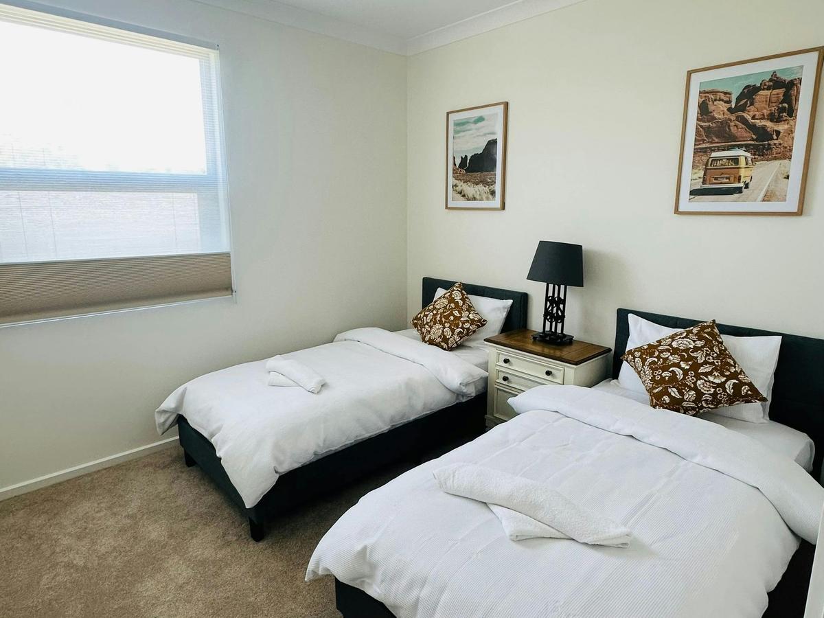 Bedroom with two single beds, framed artwork and a window with blinds.