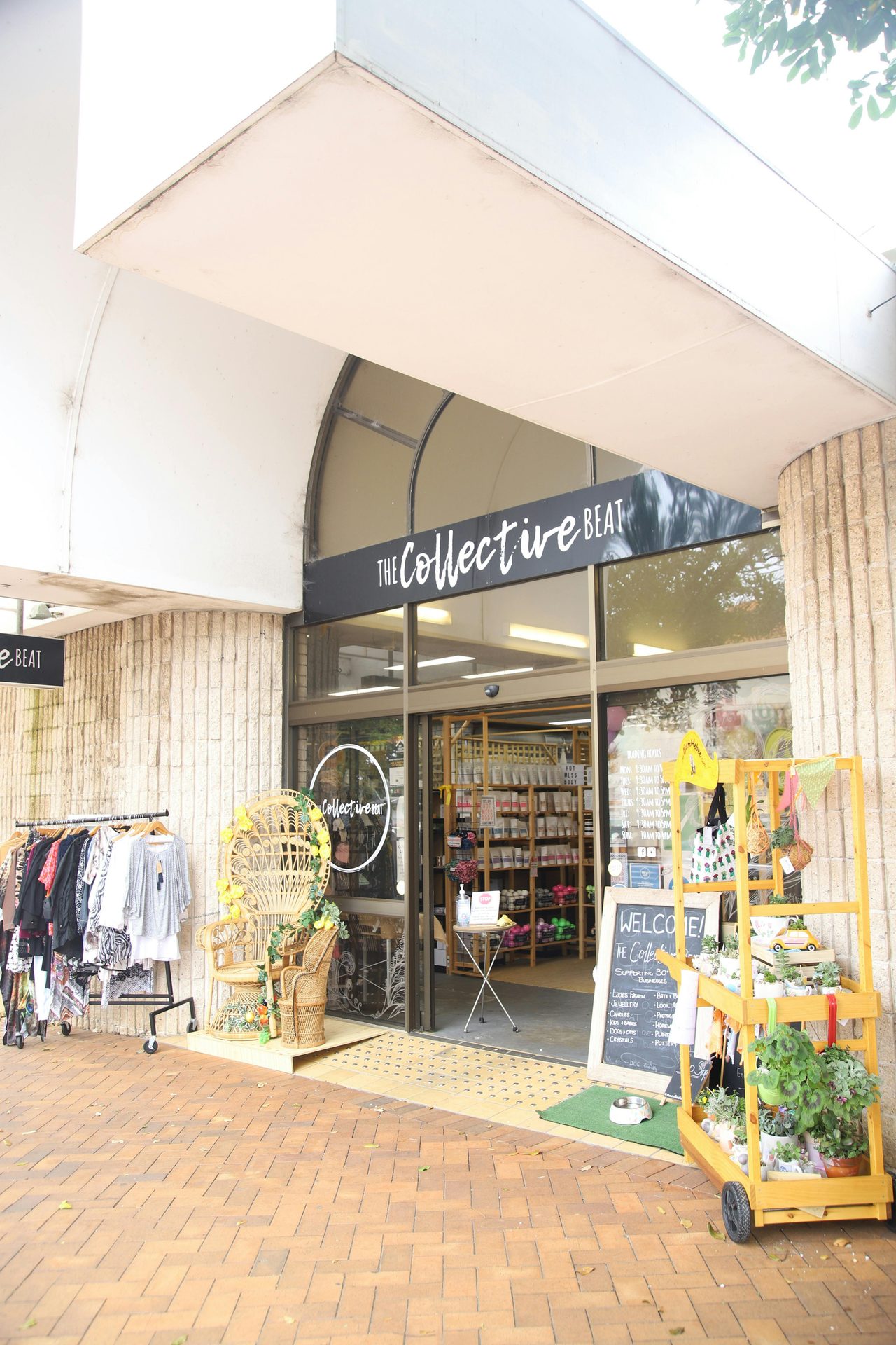 Building with the words The Collective Beat. A clothes rack, cane chair and plants out front