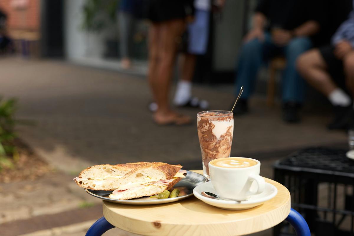 A ham and cheese baguette, flat white and cold Milo out on the stoop
