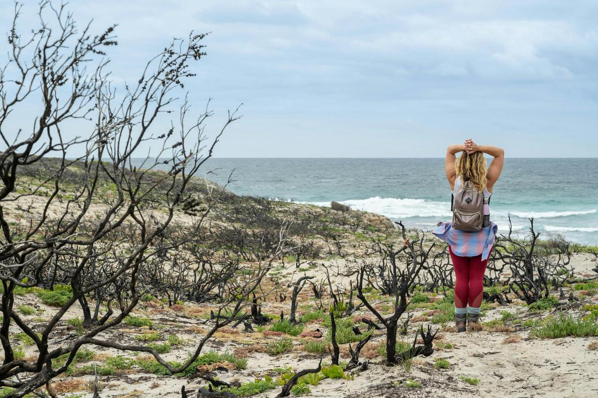 A woman stretches and looks over the coastline along the Kangaroo Island Wilderness Trail