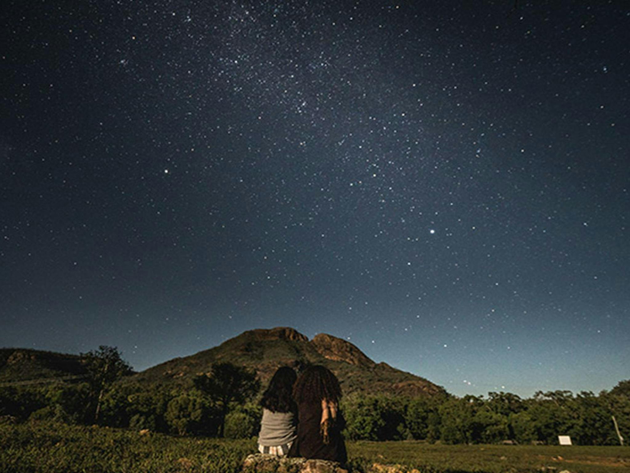Two women sit side-by-side, stargazing in Warrumbungle National Park. Photo: Robert Mulally/OEH