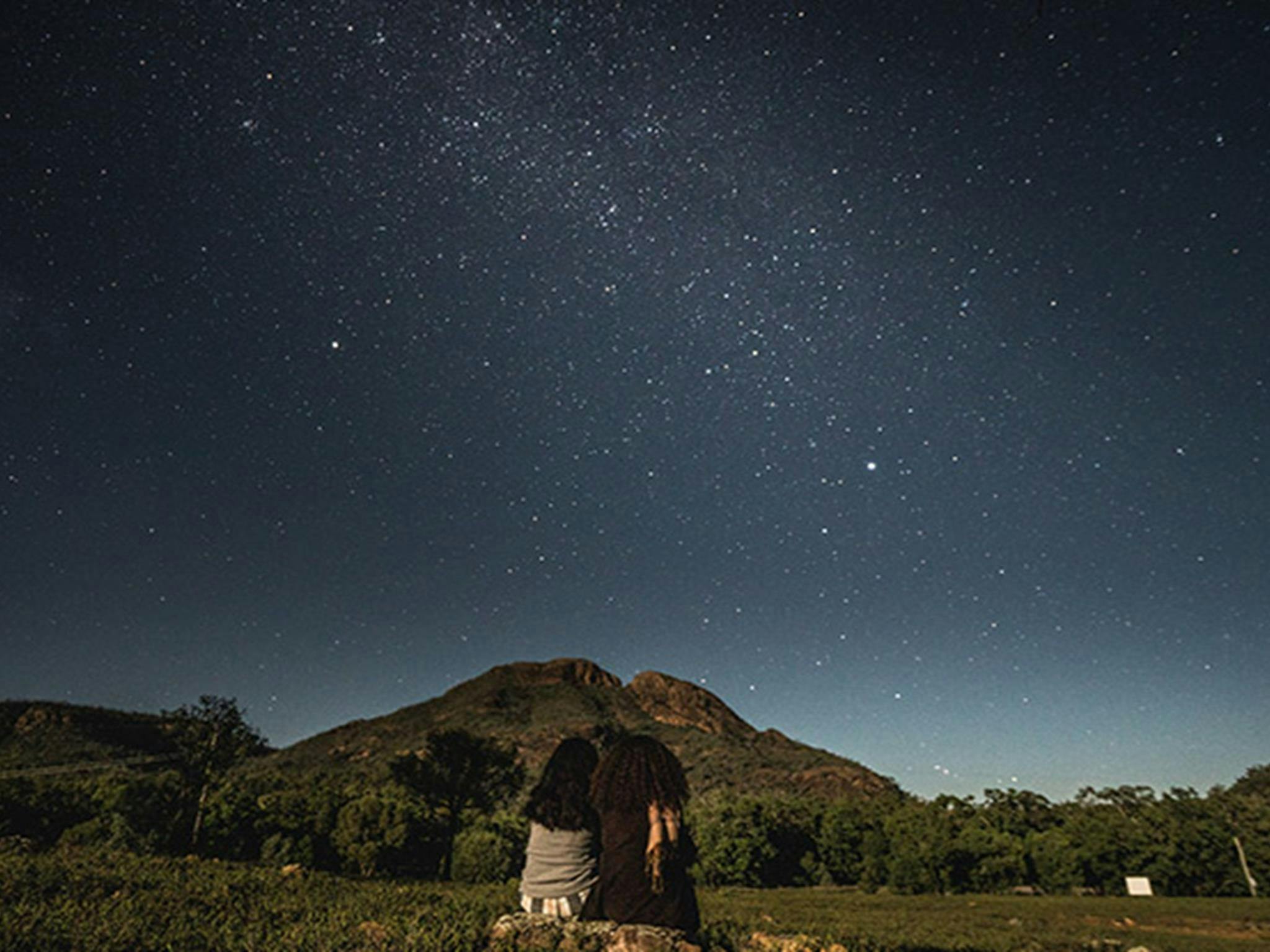 Two women sit side-by-side, stargazing in Warrumbungle National Park. Photo: Robert Mulally/OEH