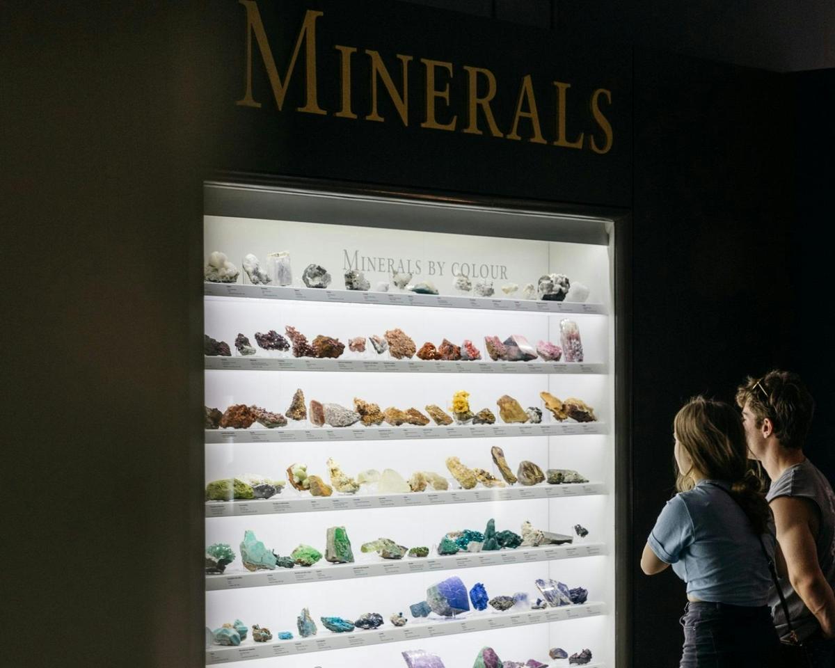 Two people stand in front of the rainbow wall of minerals display