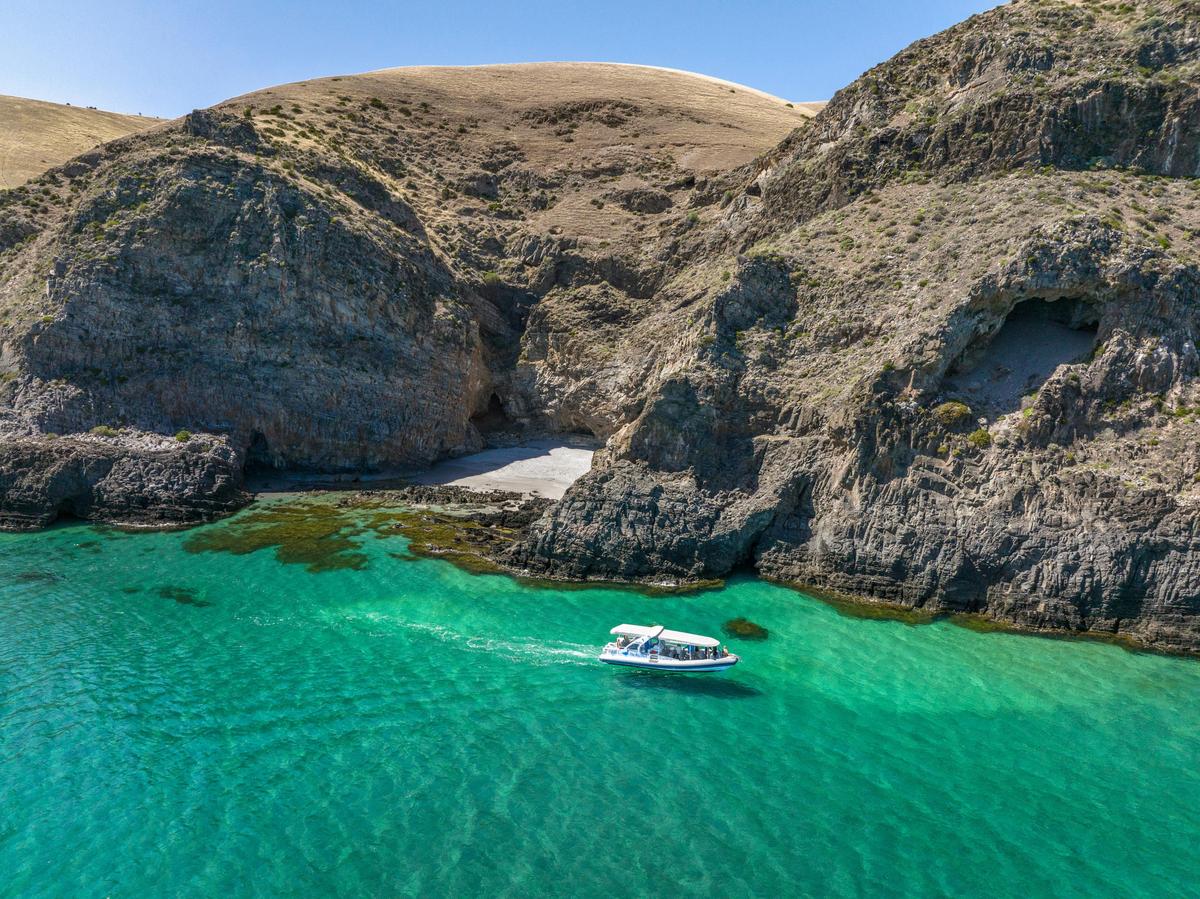 A boat cruises on clear turquoise water near a rocky shoreline and small sandy cove.