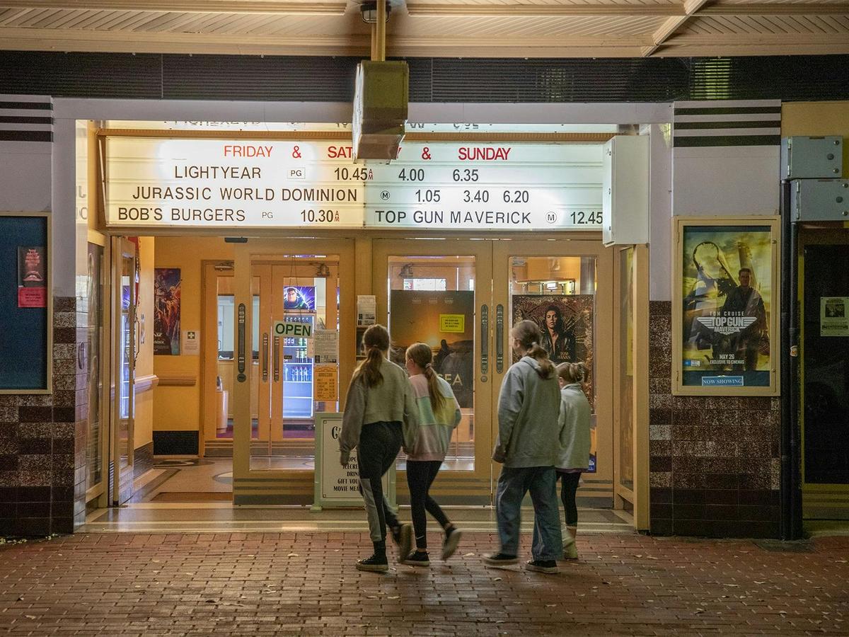 A group of 4 youth enter the front of the cinema building.