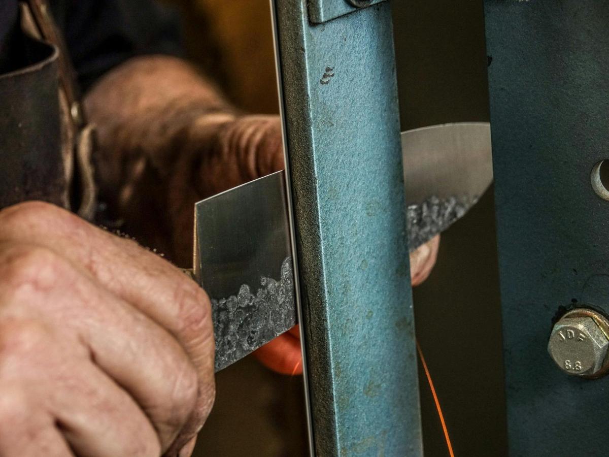 Gardner Knives knifemaker grinding knife for sharpness.