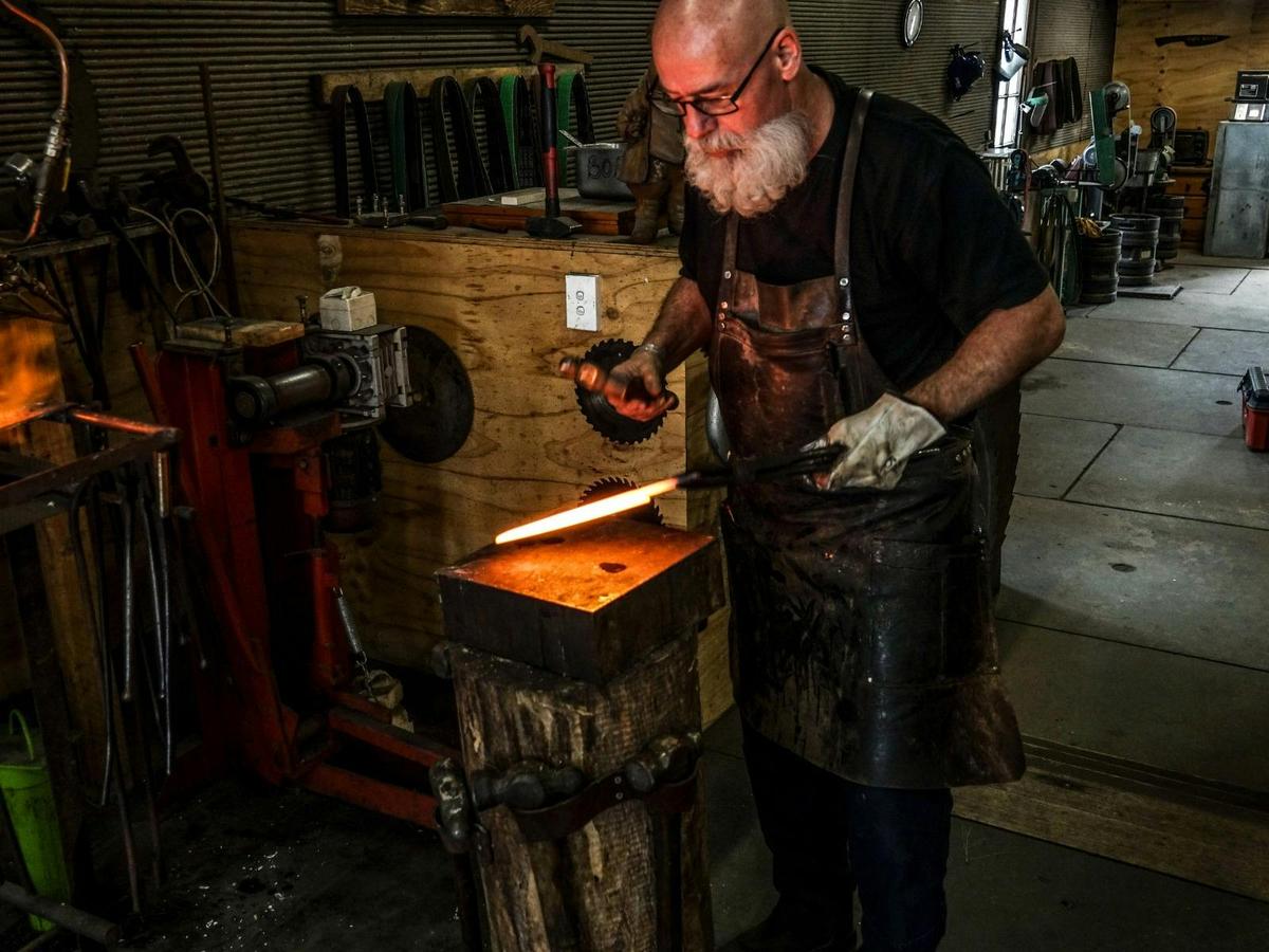 Lead bladesmith, Barry Gardner, using a hammer and anvil to shape hot steel into a knife.