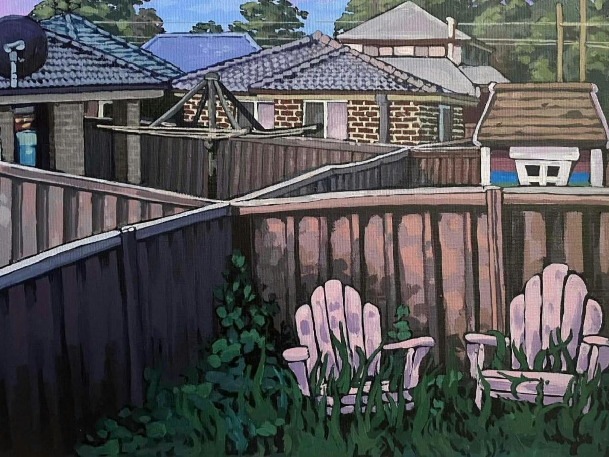 View over suburban backyards. Includes fences, outdoor chairs, clothes line, grass, roofs of houses