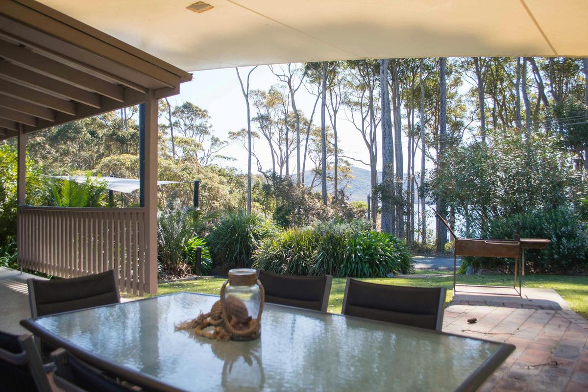 Large outdoor BBQ area is shaded by a canvas sail and is set in a tropical landscaped garden.