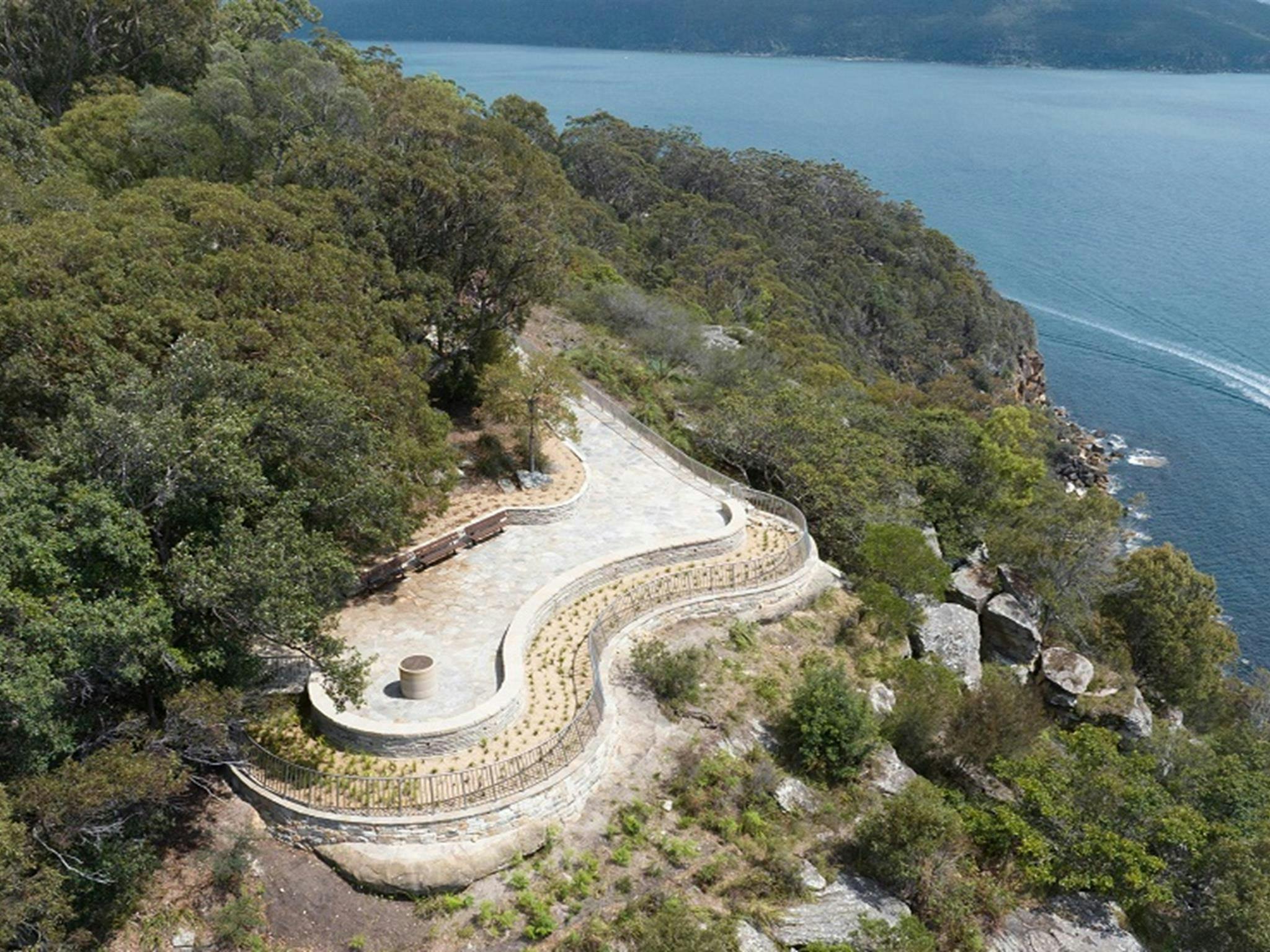Aerial view of the curved West Head lookout, at the edge of a cliff above calm water below. Credit: