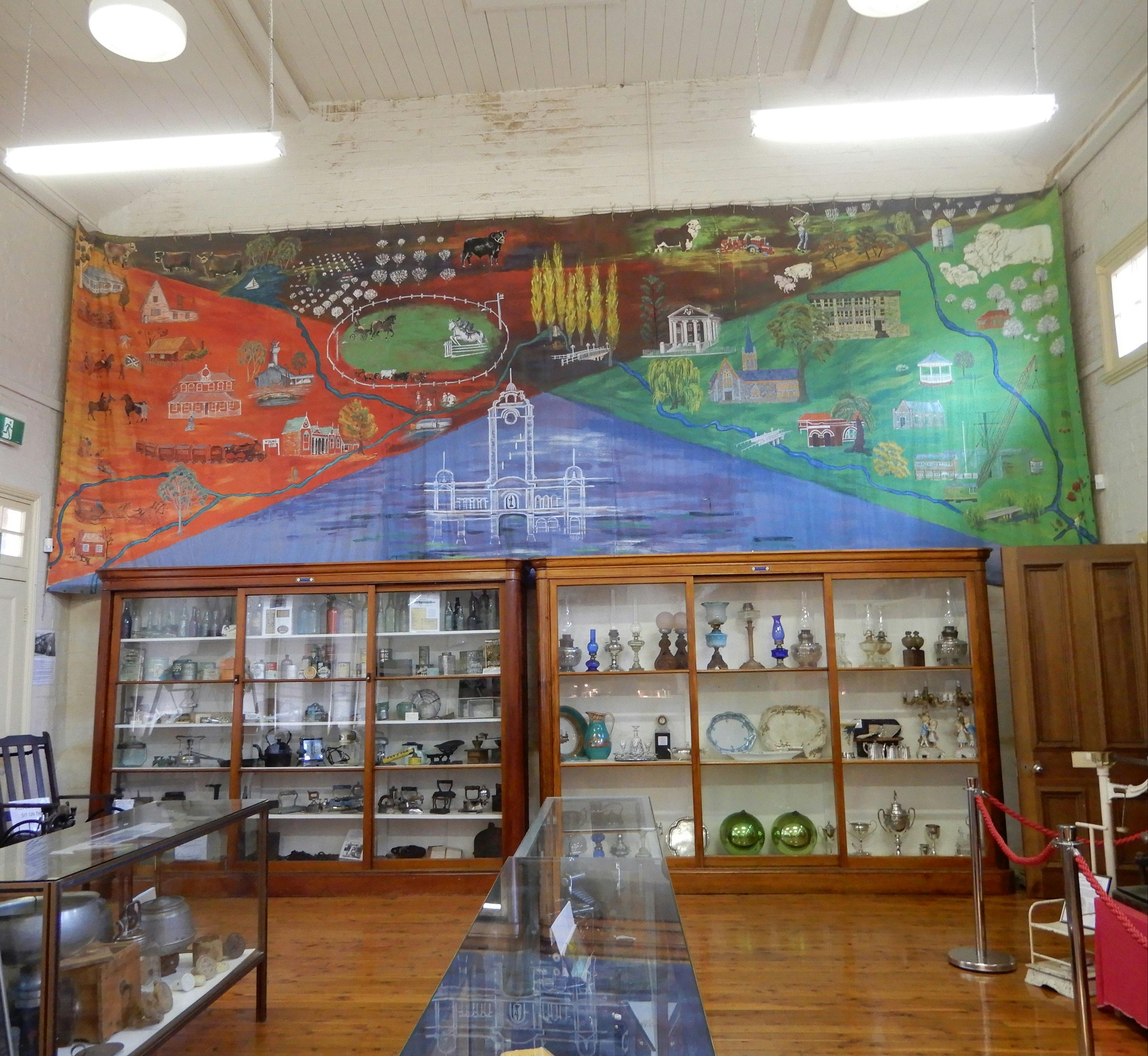 Big mural with historical buildings & farmland in Young, above an antique appliance & glass display