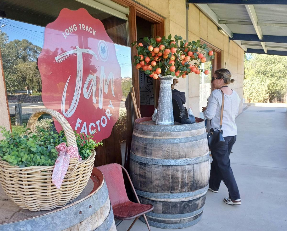 A woman walking into Long Track's Jam Factory. Barrels have floral displays on top to welcome.