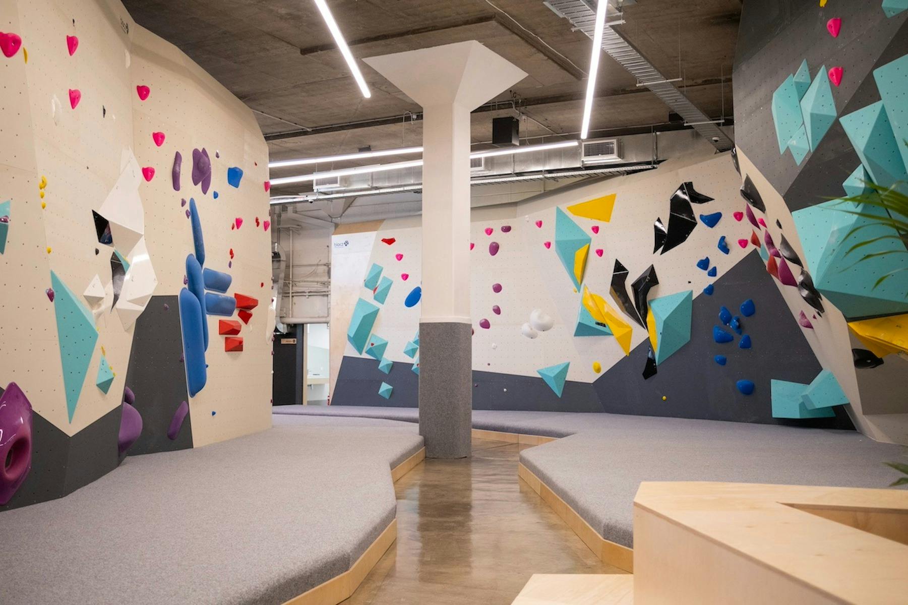 a wide shot of the colourful walls and grey matting of a bouldering gym