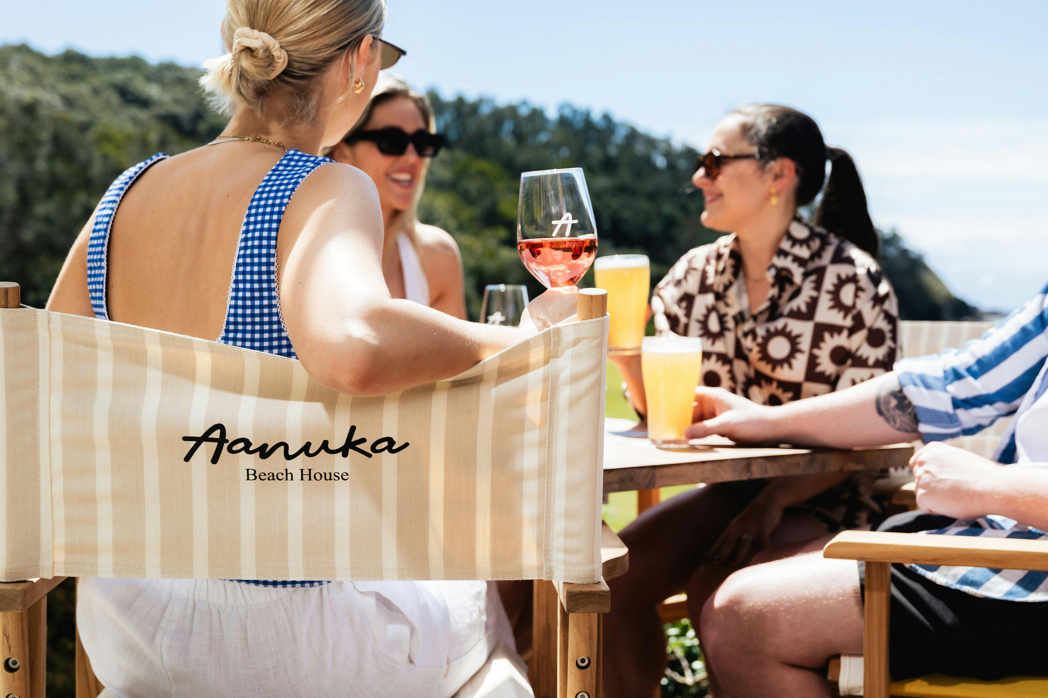 group of friends enjoying drinks outside on Aanuka Beach House branded deck chairs