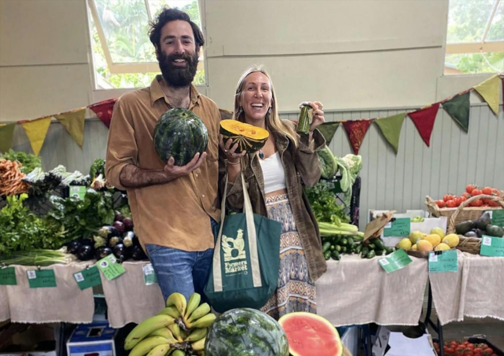 Two market customers holding up organic produce