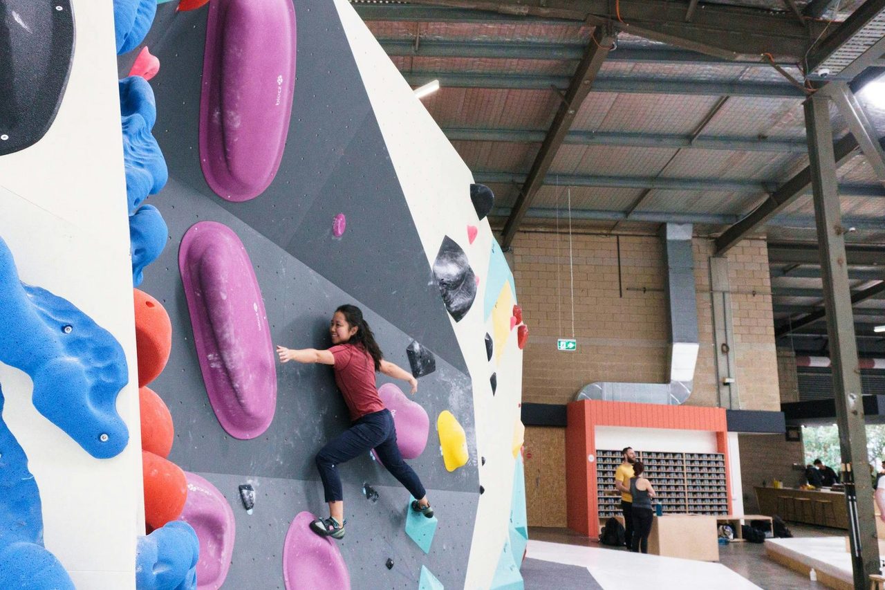 a climber is smiling, on the wall amongst large purple holds