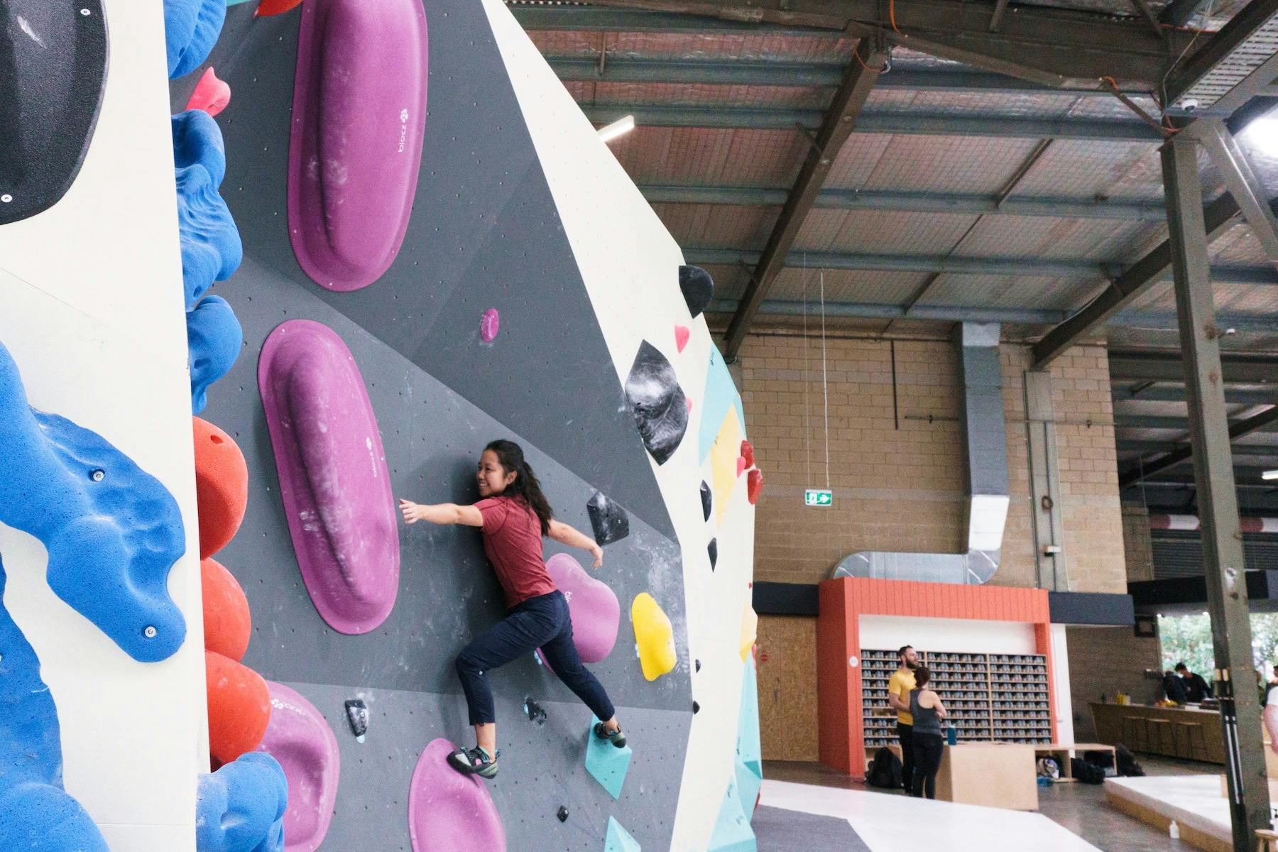 a climber is smiling, on the wall amongst large purple holds