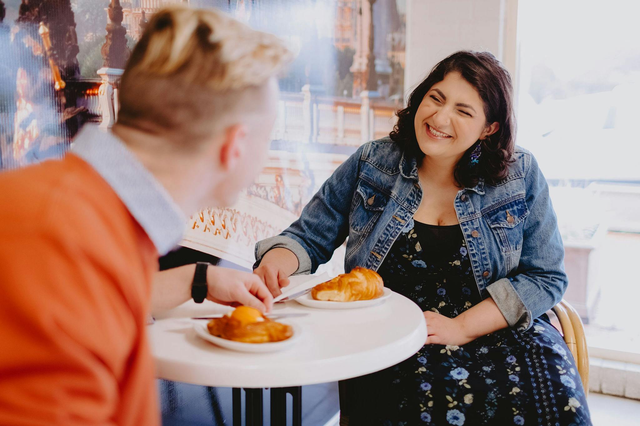 A young couple sitting at a cafe table at The Artisan Baker laughing and enjoying pastries together.