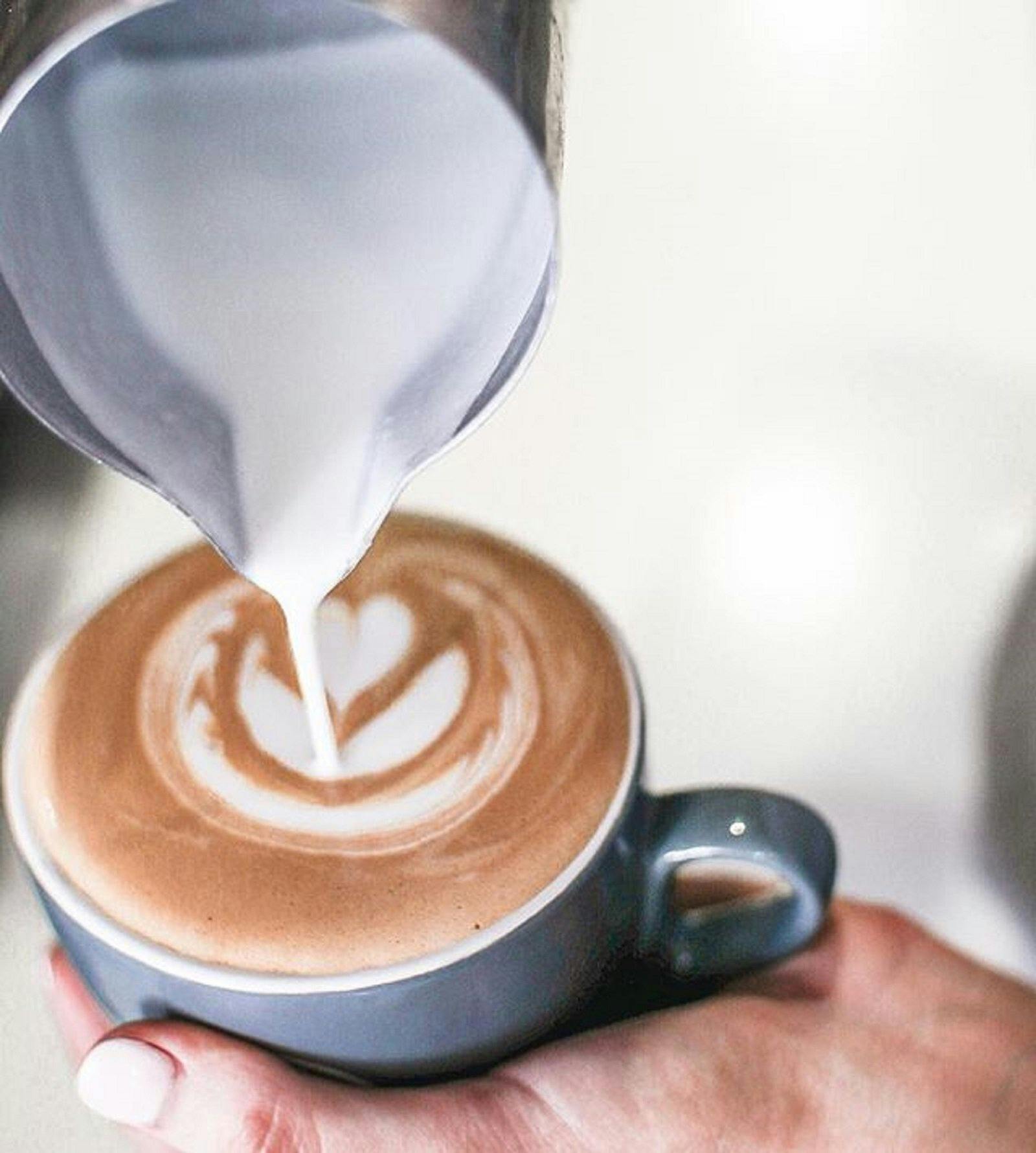 A hand pouring out milk in a cup of coffee