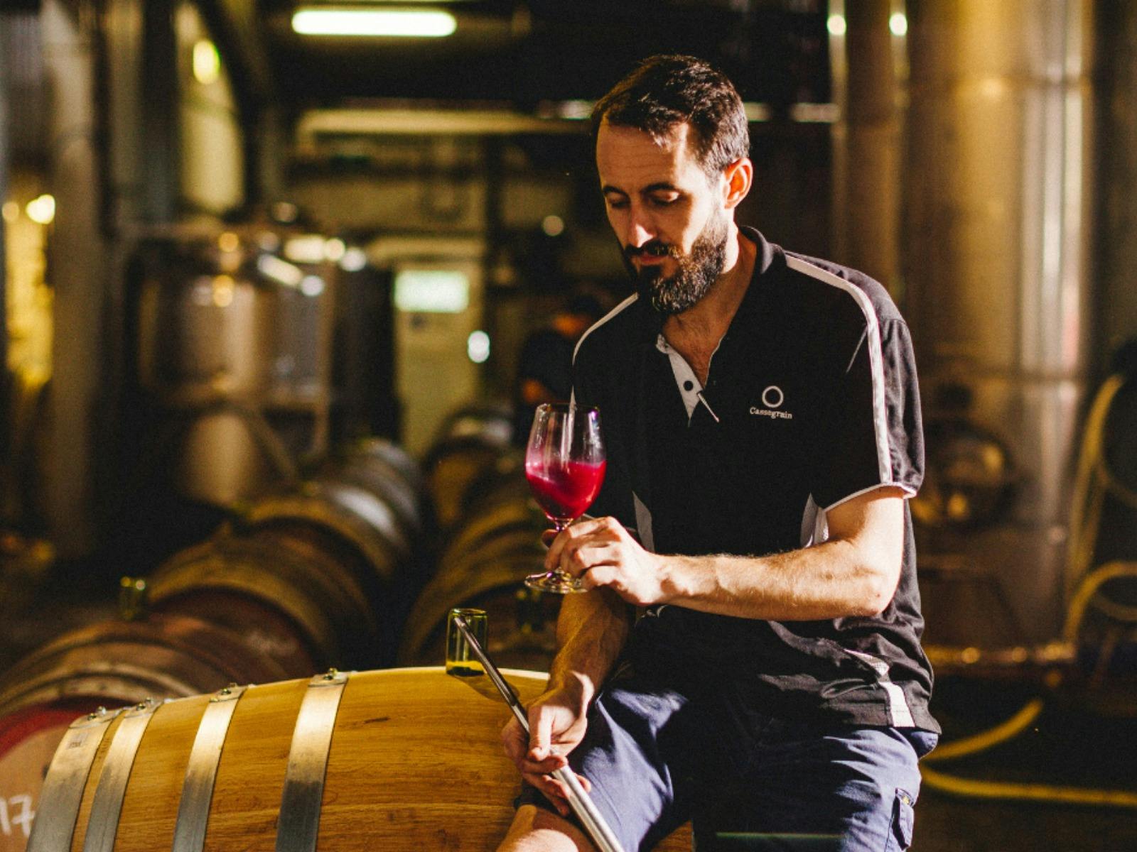 Alex Cassegrain leaning against a wine barrel tasting wine