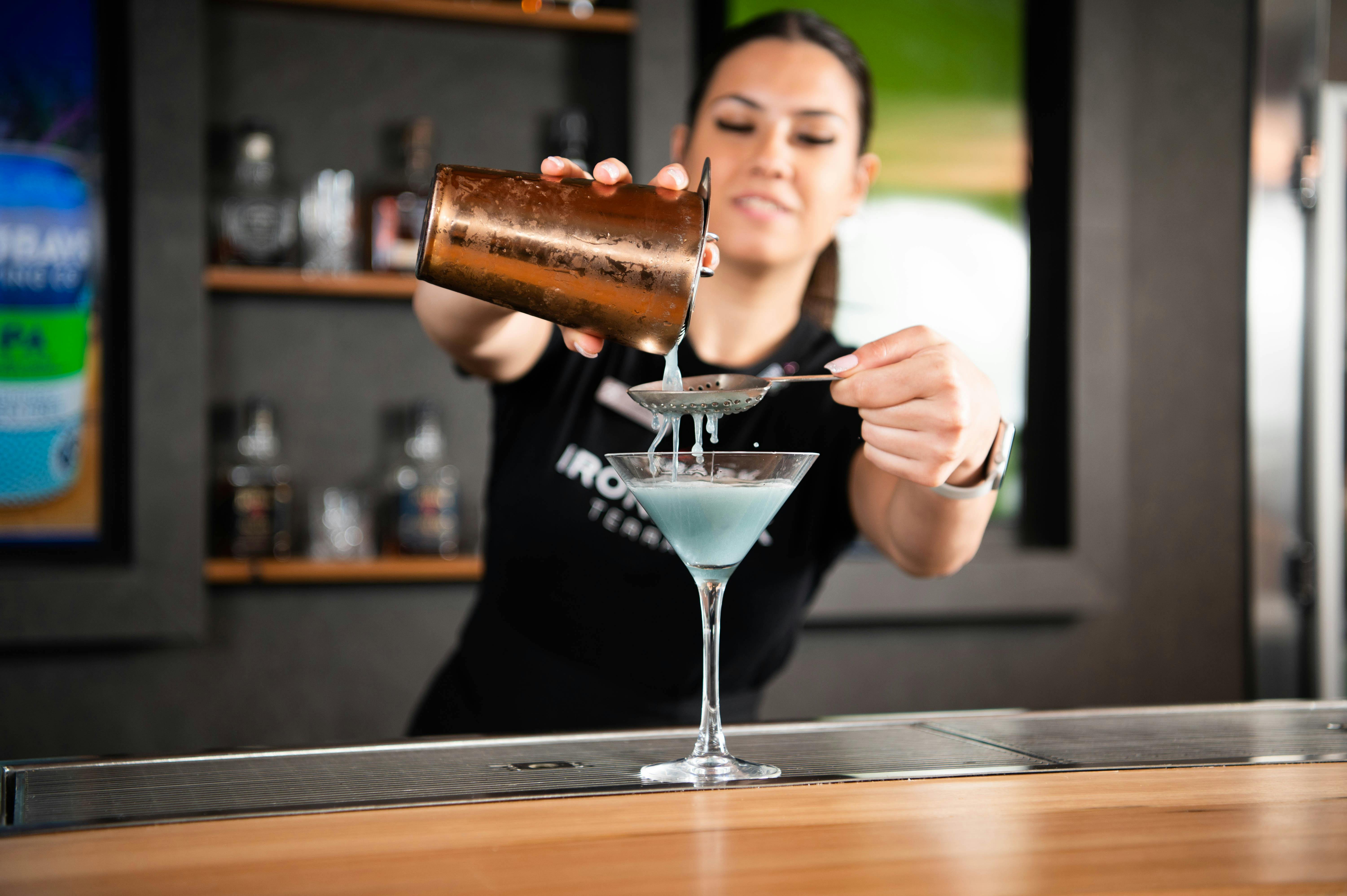 woman pouring cocktail into martini glass