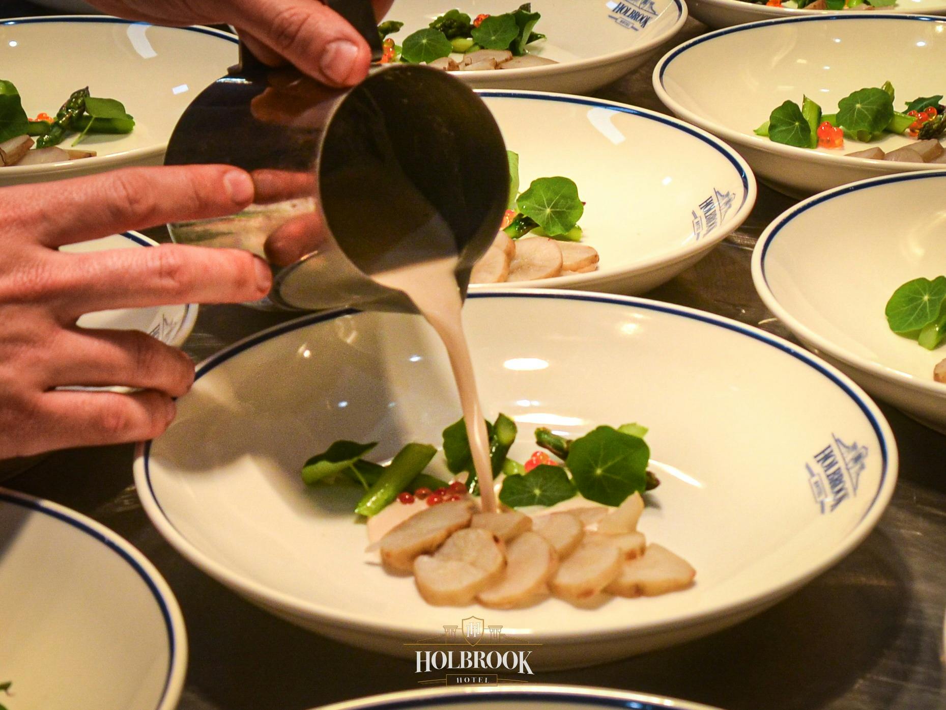 Sauce being poured on a meat and veg dish in a white bowl