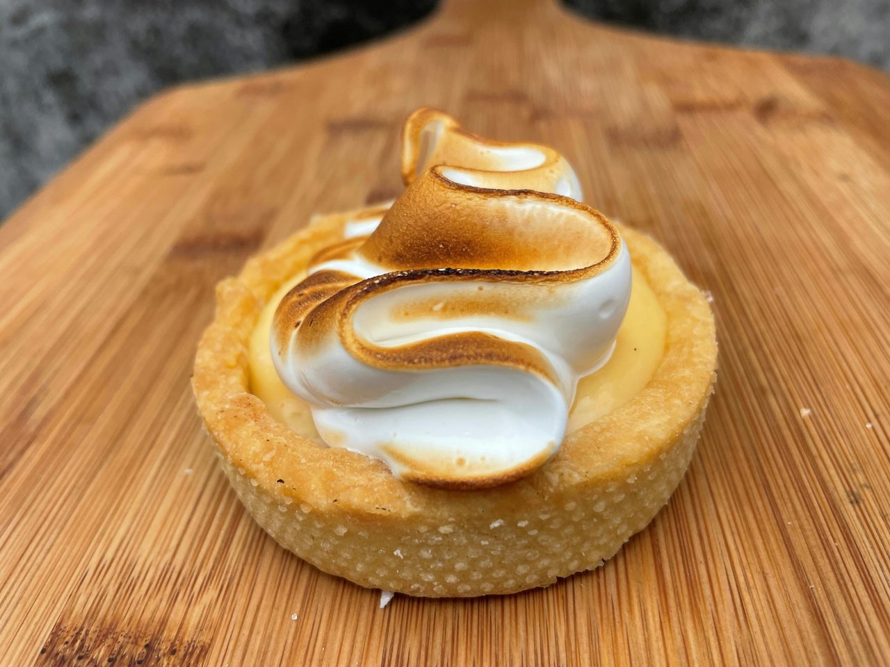 A single Lemon Meringue Tart displayed on a wooden board