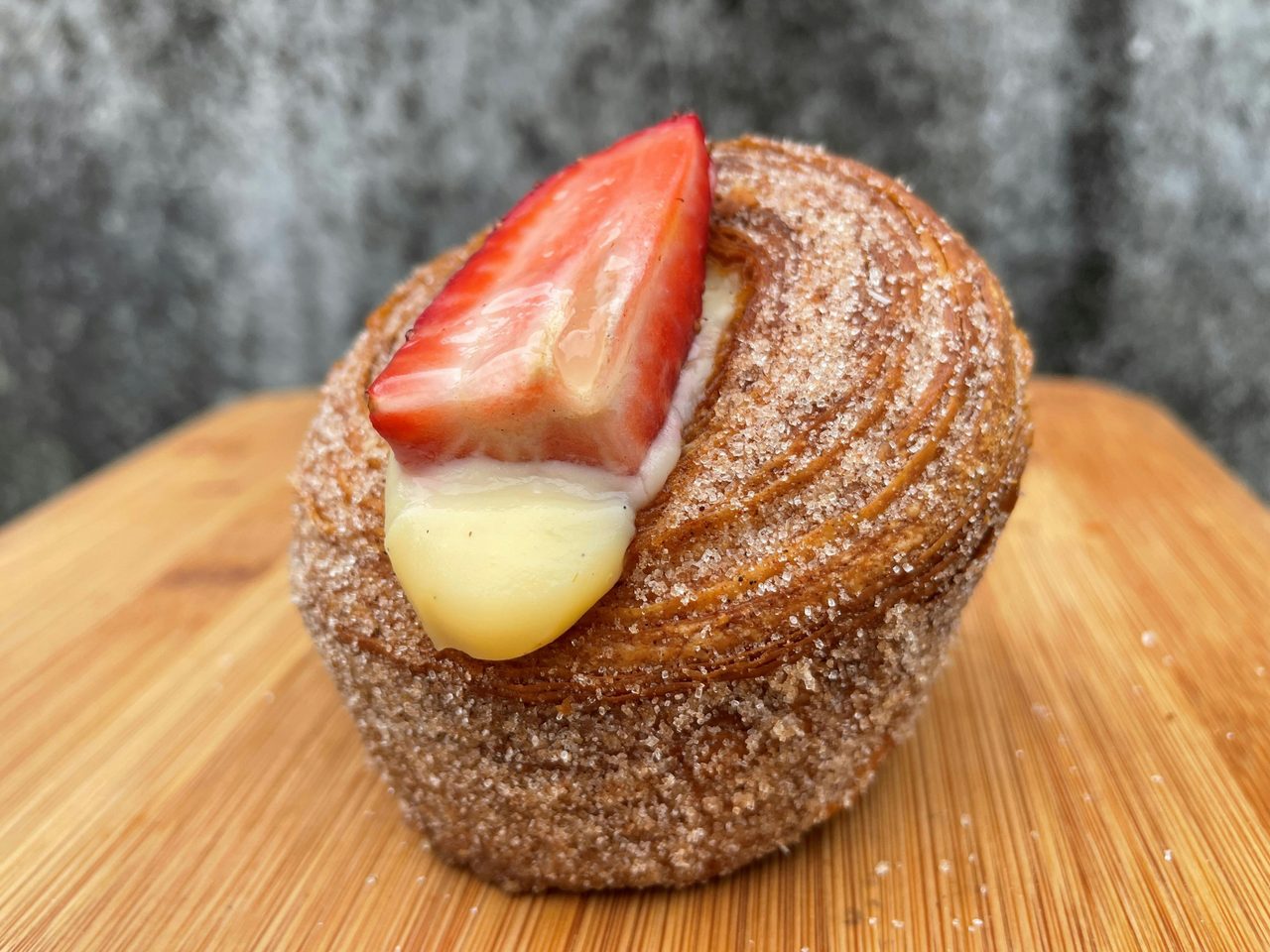 A single cruffin covered in cinnamon sugar, filled with fresh custard and topped with a strawberry