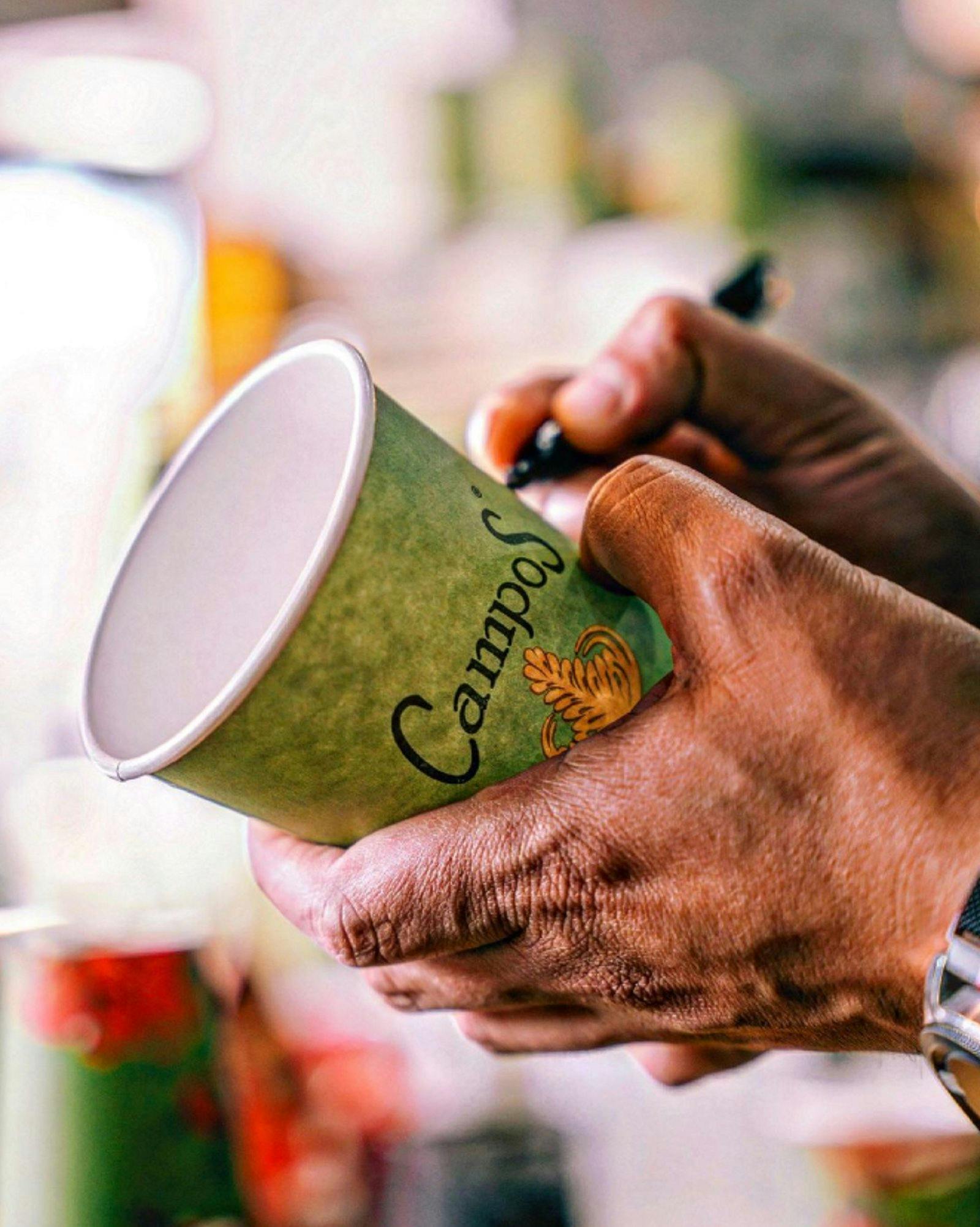 Hand holding up a coffee cup and writing words on it with a texter