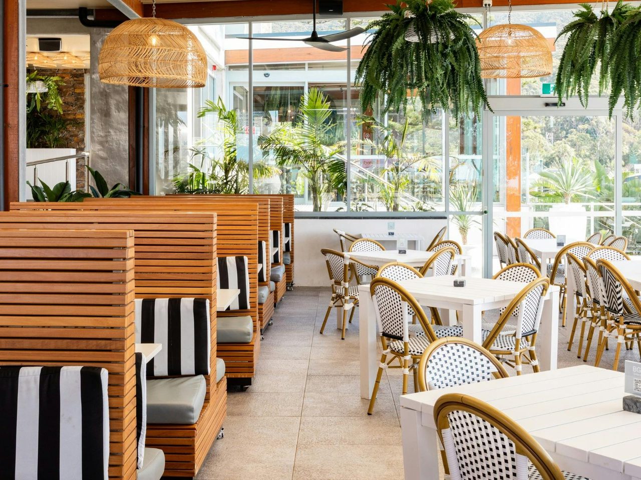 Bright dining area at Headlands Austinmer Beach with booths, plants and rattan lights.