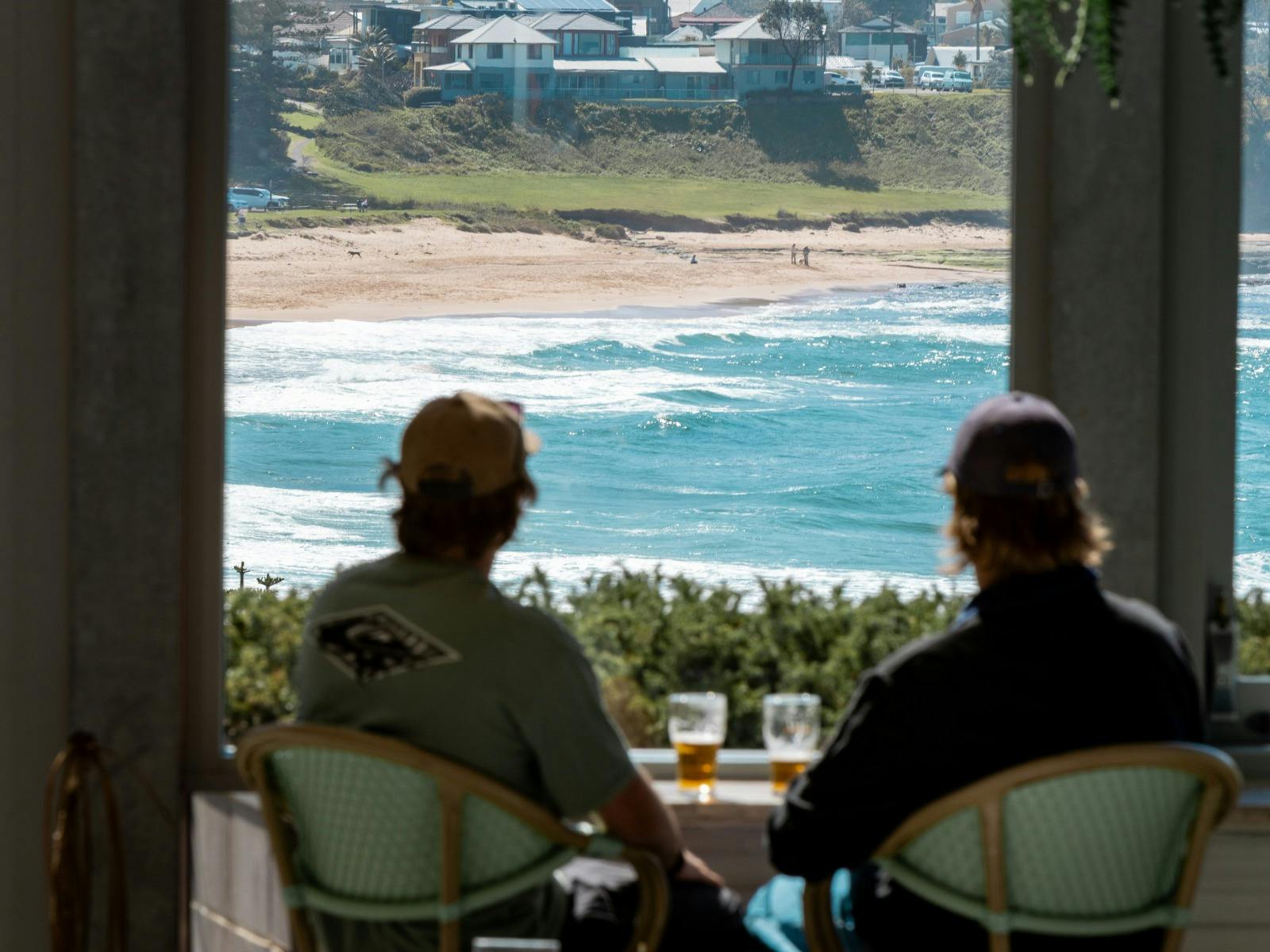 Two people sitting with beers at Headlands Austinmer Beach, overlooking the ocean.