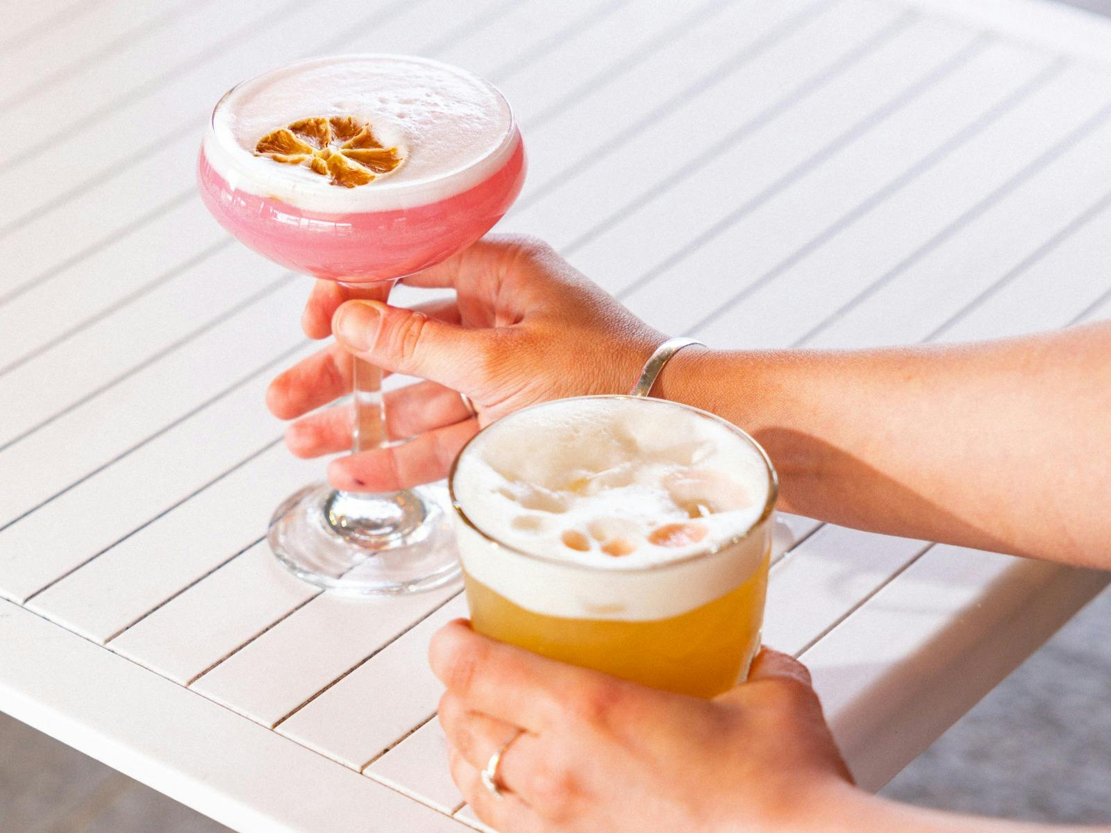 Close-up of hands holding pink and orange cocktails.