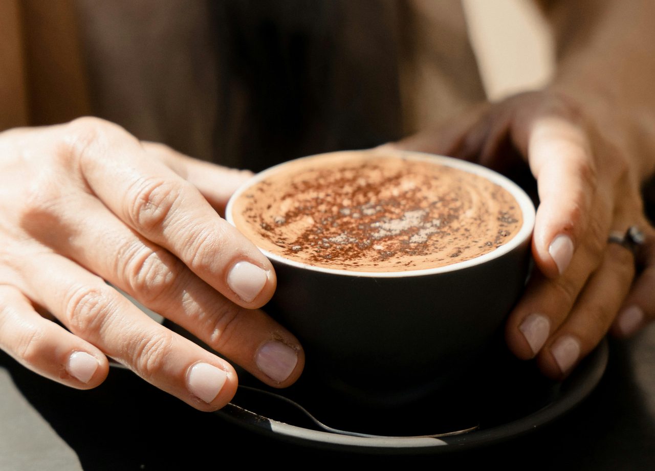 A man holds a cup of cappuccino in his hands.