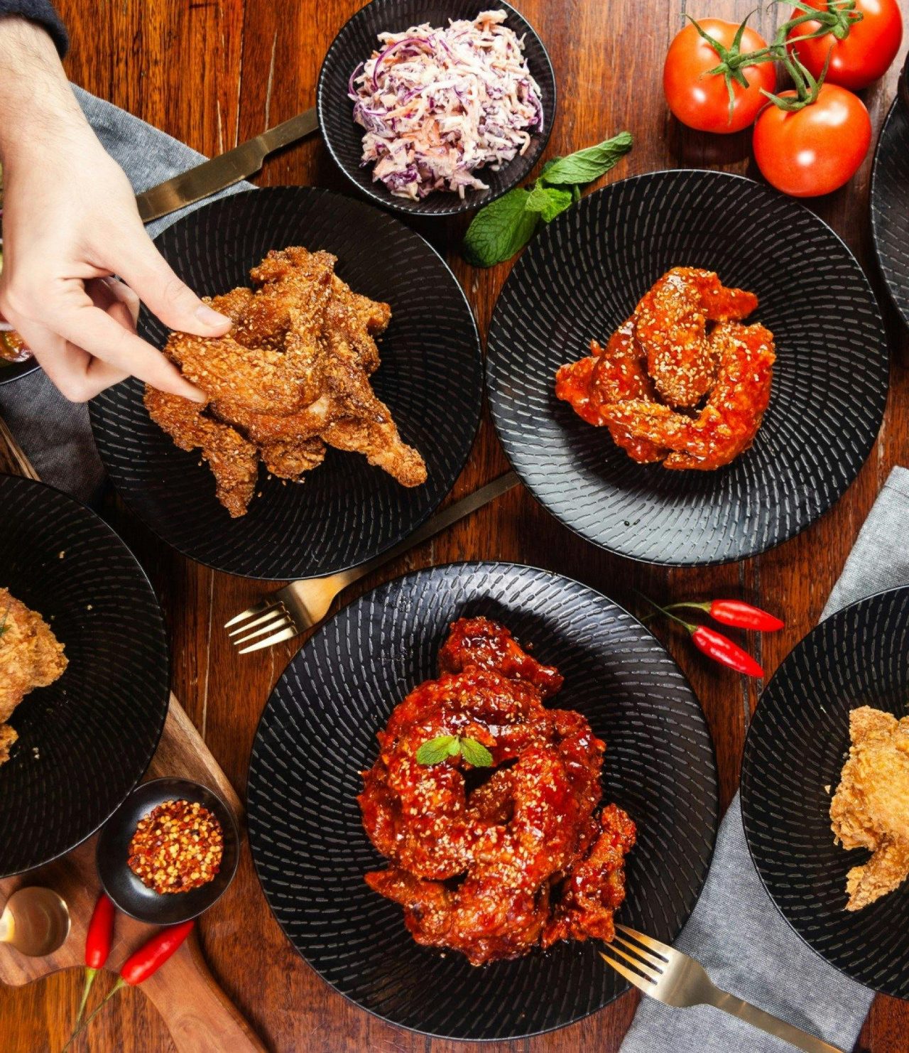 Hand holding a piece of Korean fried chicken with other plates of fried chicken pieces