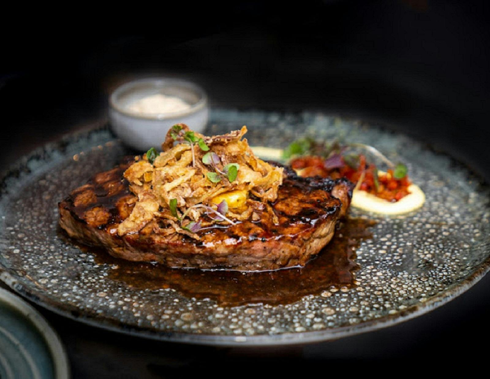 A piece of steak on a place with garnish and sauce on the side