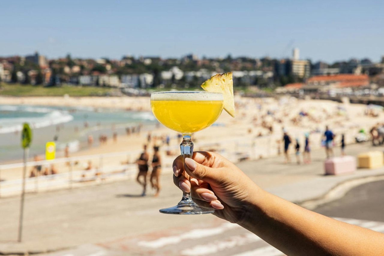 Hand holding cocktail in front of beach