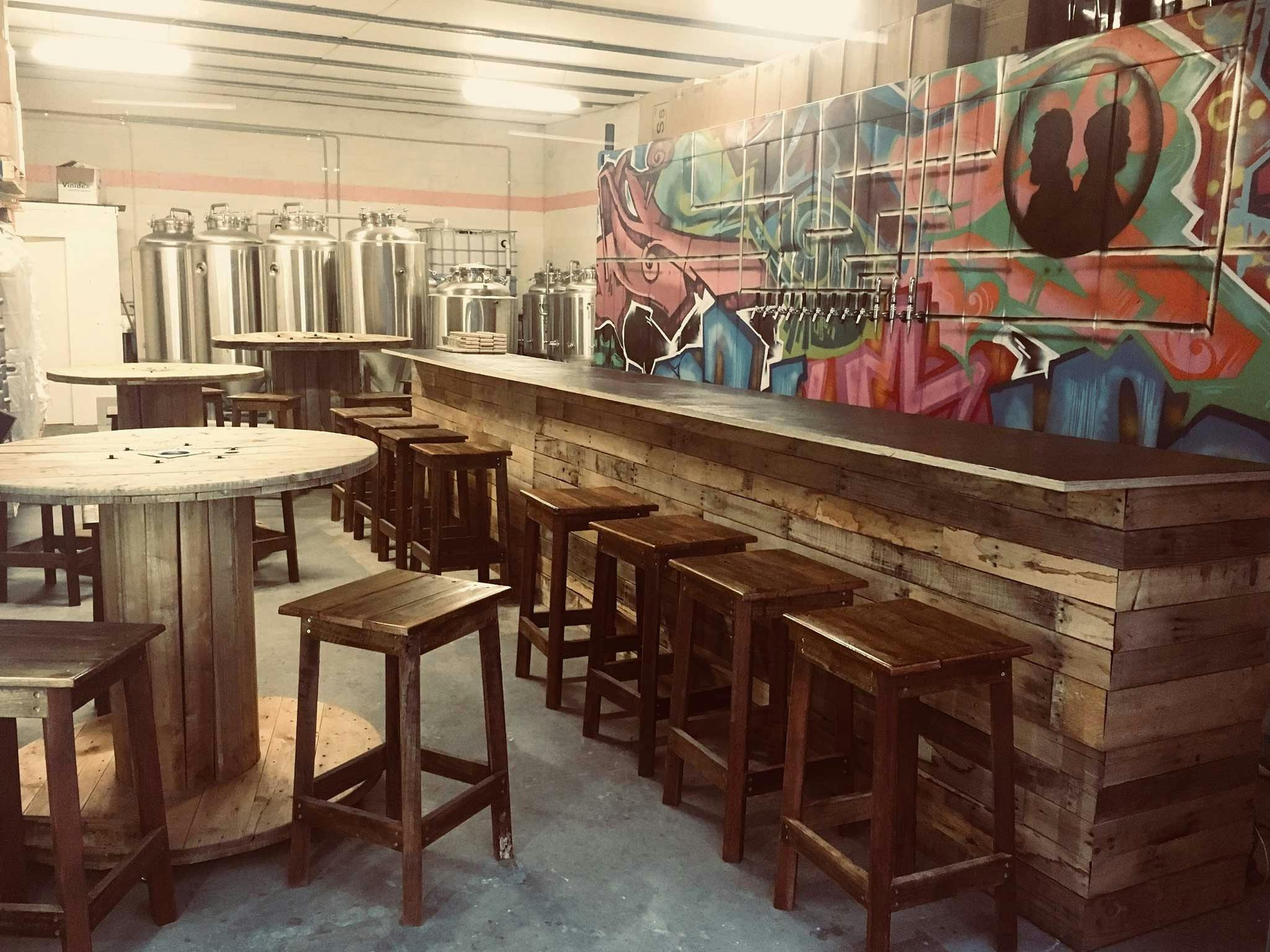 Wooden tables and bar with brewing tanks and graffiti mural behind