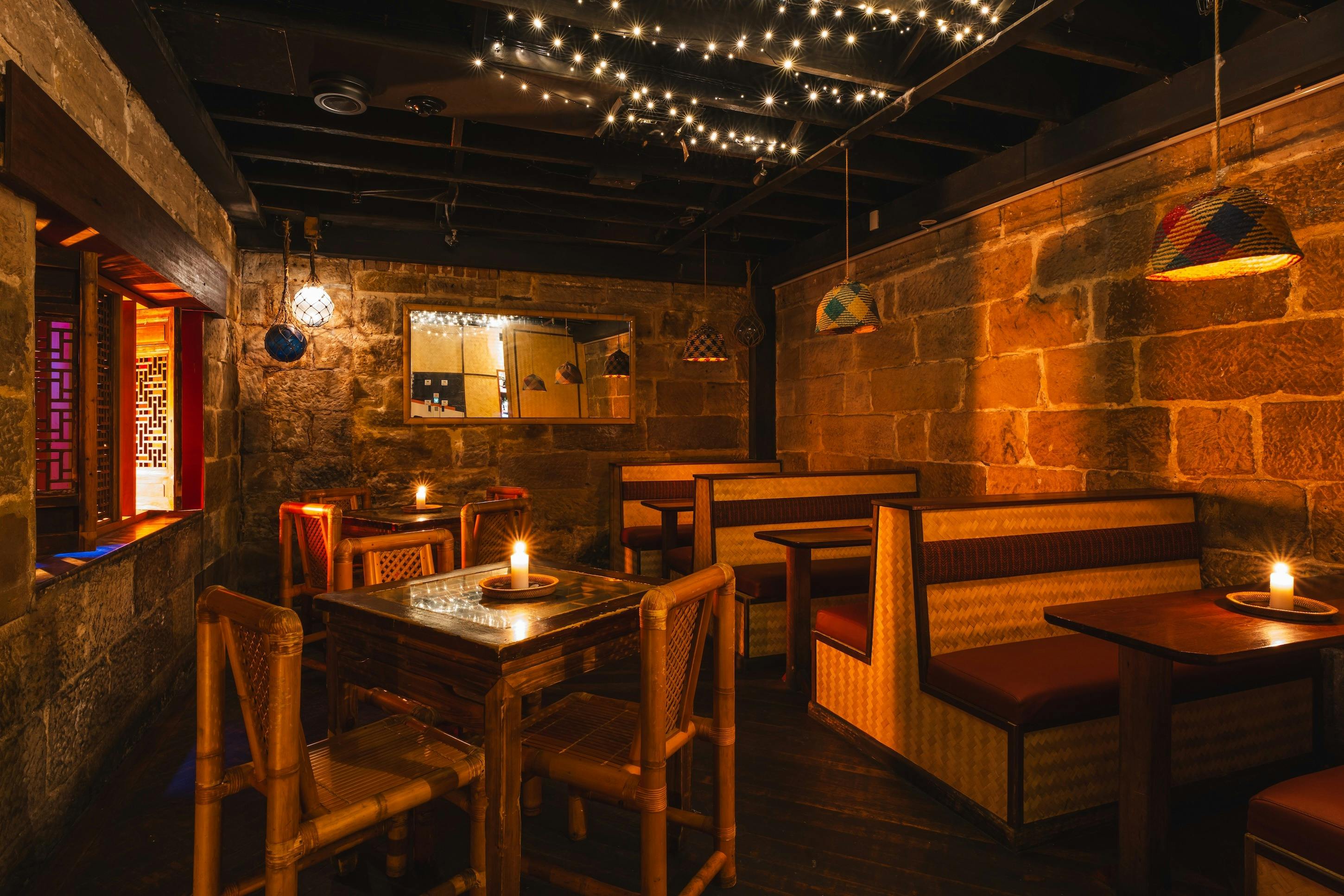 Warm lounge with stone walls, bamboo chairs, booth seating, hanging lamps, and fairy lights